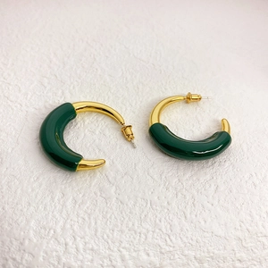 Detail of chunky C-shaped hoop earrings featuring gold metal and deep green enamel finish