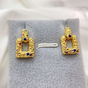 Detail of gold rectangular earrings with lava texture and multi-color crystal stones