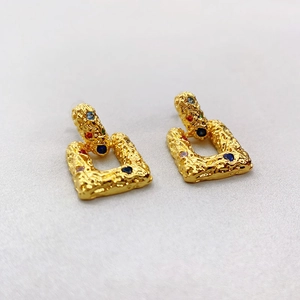 Detail of vintage gold earrings featuring irregular lava texture and colorful gemstones