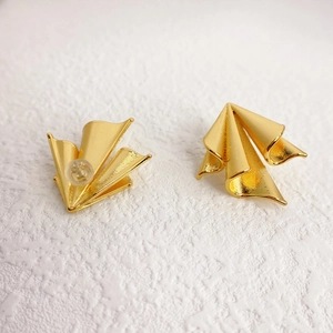 Fashionable gold airplane-inspired stud earrings with textured satin finish on white surface