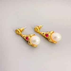 Conch style gold pearl drop earrings with red gemstone accents on gray background