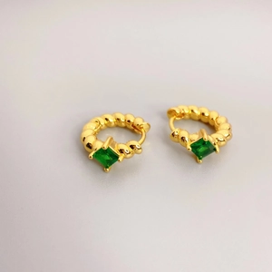 Macro shot of gold hoop earrings with green square gemstones and rope texture