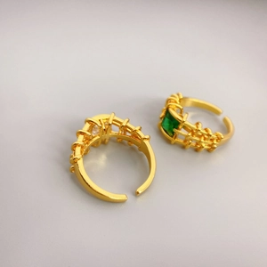Detailed close-up of gold rings featuring emerald and zircon stones with hollow mesh bands