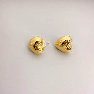 Polished gold heart stud earrings with silicone backs on a minimalist gray background