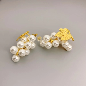 Golden leaf and pearl grape cluster earrings on a neutral background for fashion