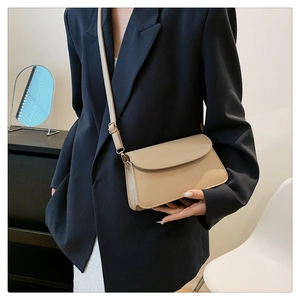 Detail of minimalist beige flap crossbody bag with adjustable strap on a navy blazer