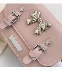 Close-up of pink crossbody bag featuring a silver metal bow and fine stitching details