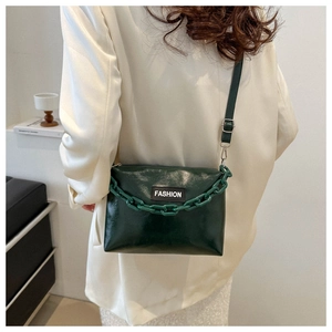 Detail of dark green glossy leather crossbody bag with bold chain and fashion label