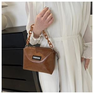 Detail of caramel faux leather bag featuring a fashion patch and thick chain strap