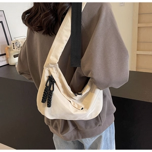 Detail der cremefarbenen Nylon-Halbmondtasche mit schwarzen Riemen am Model im Café