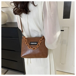 Brown faux leather shoulder bag with acrylic chain and Fashion text on a model