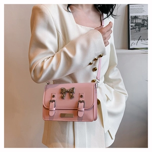 Pink crossbody square bag featuring silver bow detail and dual leather buckles on a model