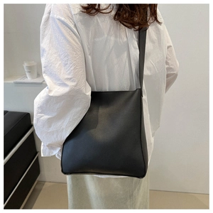 Detailed side view of a minimalist black matte leather crossbody bucket bag on a model