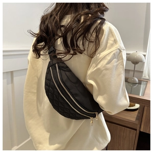 Detail of black quilted waist bag with three golden zippers shown worn by a model