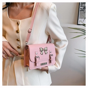 Close-up of pink crossbody bag with metal bow accent and decorative straps on model