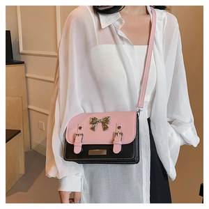 Detail view of pink and black crossbody bag with gold bow on a stylish model