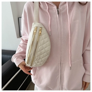 Close-up of cream quilted chest bag featuring dual gold zippers and wide strap detail