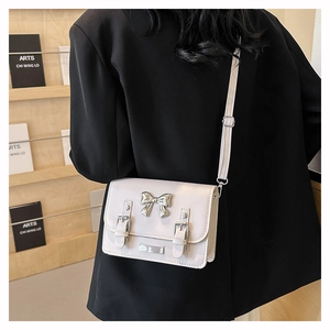 Close-up of white crossbody bag with silver bow accent and buckle straps on black blazer