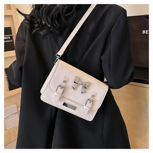 Detail view of cream crossbody bag featuring a silver metal bow buckle and buckle straps