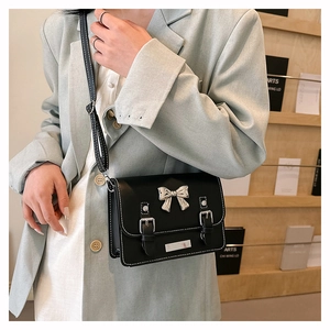 Detail of black crossbody messenger bag with silver bow accent and leather straps