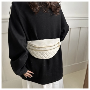 Detailed close-up of a quilted cream nylon fanny pack with golden zippers on a model