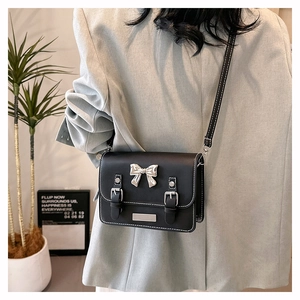 Detail of black crossbody bag with silver bow buckle and white stitching on grey blazer