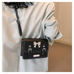 Detail of black crossbody bag featuring silver bow accent and white contrast stitching