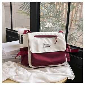 Sac messager en toile contrastée avec détails bordeaux pour femme sur une petite table