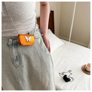 Detail of mini orange mirror crossbody bag with silver butterfly and metal chain
