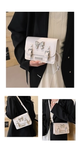 Detail view of white square flap bag featuring silver metal bow and buckle decorations