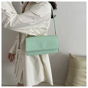 Side view of mint green woven leather baguette bag on model with slim shoulder strap