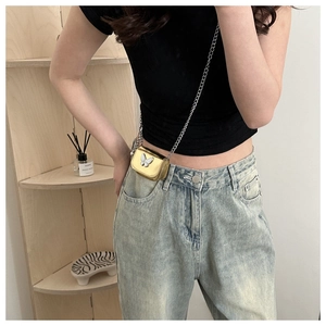 Close-up of golden mini crossbody bag with white butterfly charm and silver chain strap