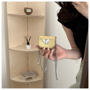 Close-up of golden mini crossbody bag with white butterfly detail and silver chain strap