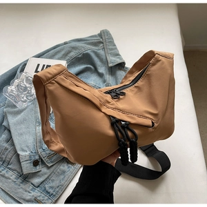 Khaki brown nylon crescent bag with wide black strap and rope detail in a casual setting