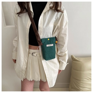Detail of green corduroy phone bag featuring a yellow snap button and wide brown strap