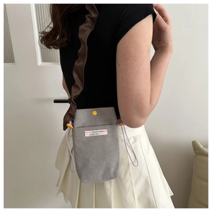 Detail of greyish-purple corduroy phone bag with ruffled brown strap and decorative label