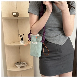Detail of light green corduroy crossbody bag with purple ruffled strap and orange drawstring