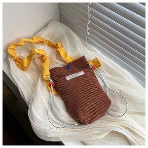 Detail of brown corduroy phone bag featuring vibrant yellow ruffled strap and woven label