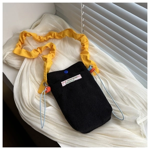 Detailed shot of black corduroy mini bag featuring a yellow ruffled shoulder strap
