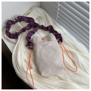 Close-up of beige corduroy phone bag with purple pleated strap and orange buttons