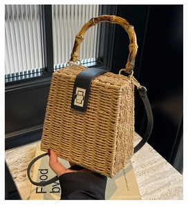 Detail of woven straw handbag featuring a bamboo handle and black leather flip cover