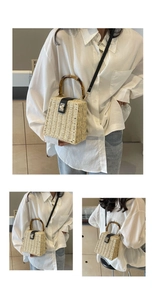 Detail of woven straw handbag featuring bamboo handles and a leather clasp closure