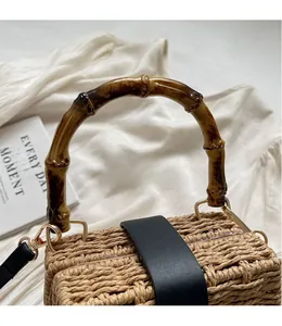 Detail of woven straw handbag featuring bamboo handles and black leather decorative strap