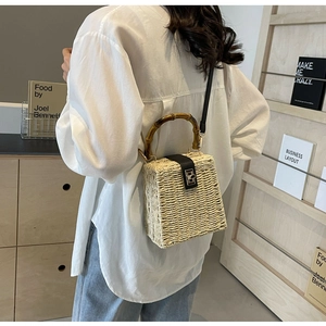 Detail view of woven straw box bag with bamboo handle and leather flap on model