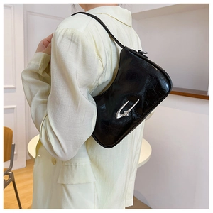 Close-up of black patent leather crescent bag with silver star buckle worn by a model