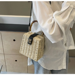 Detail of woven straw bag featuring bamboo handle and black leather flap with gold lock