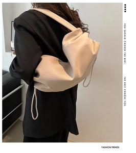 Detail view of a beige pleated canvas tote bag worn by a model on a shoulder strap