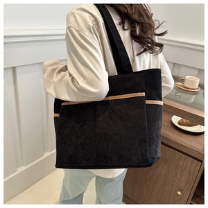 Detail showing the corduroy texture and decorative front pocket of the black tote bag
