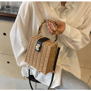 Detail of woven straw handbag with bamboo handle, leather strap, and golden twist lock