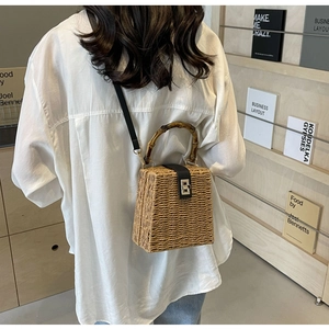 Detailed view of woven straw bag with bamboo handle and leather flap on a model